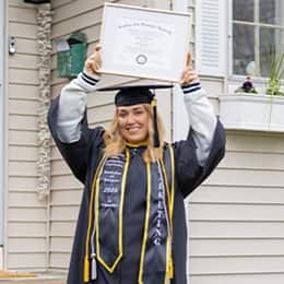 Madison Richards '26, wearing a cap and gown holding her framed diploma over her head.
