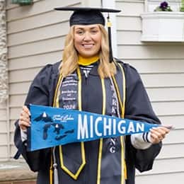 Madison Richards '26, wearing a cap and gown holding a Michigan state flag.