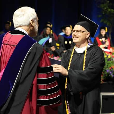 Parker Bryant wearing cap and gown and receiving his degree from SNHU President Paul LeBlanc.