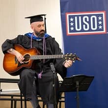 Nate Lohn playing his guitar in front of USO sign 