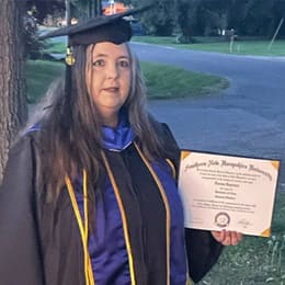 Norma DePriest dressed in a graduation cap and gown, holding her SNHU diploma.