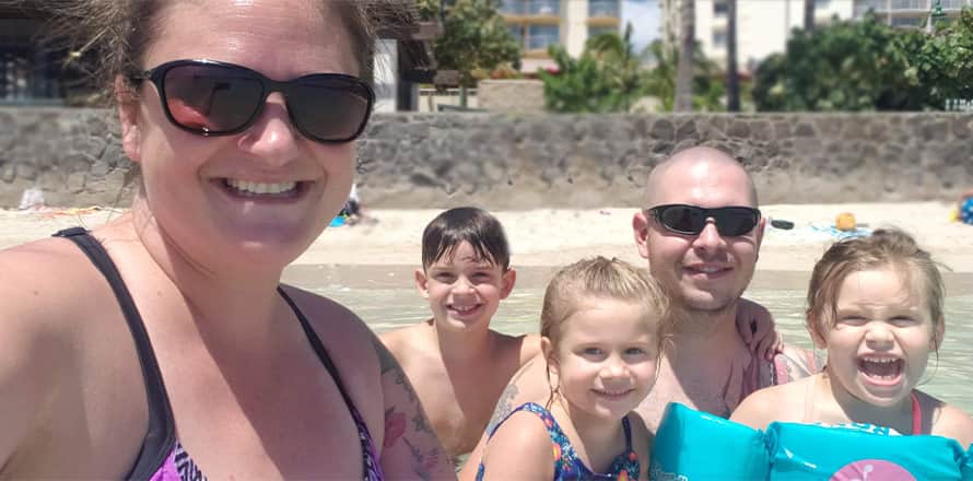 A selfie of Heather Poss with her husband and three children standing in the water at the beach