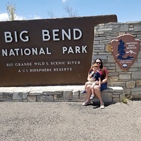 Tara and her son sitting in front of Big Bend National Park sign 