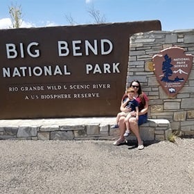 Tara and her son sitting in front of Big Bend National Park sign