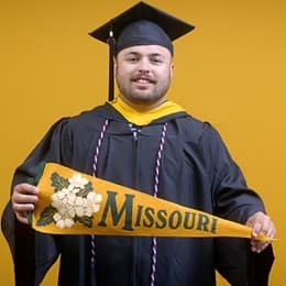 Payton Good, a 2025 SNHU graduate who earned his bachelor's in operations management wearing his cap and gown in front of a yellow background, holding a Missouri state flag.