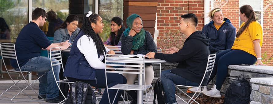 A group of people from diverse backgrounds and genders sitting at an outdoor table.