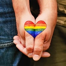 Two hands holding one another with a rainbow heart in the middle