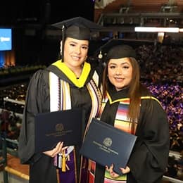 Priscilla Vega, a BS in Business Administration grad and Tiffany Garcia, an AS in Business Administration grad, holding their diplomas at their 2024 SNHU graduation.