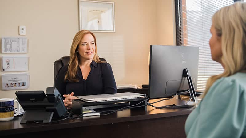 Nikki Bennett, who earned her degree from SNHU in 2022, sitting behind a desk with a phone and computer  monitor talking to another woman