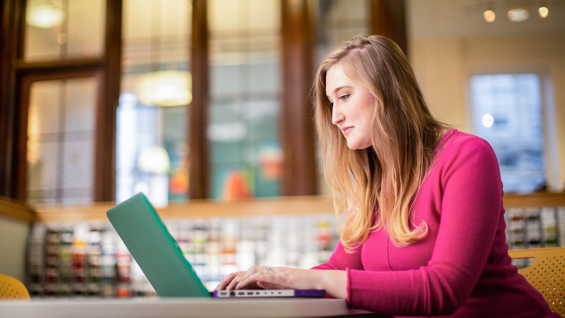 Caitlyn Carey, who earned her SNHU degree in 2015, wearing a pink sweater and working on her laptop.