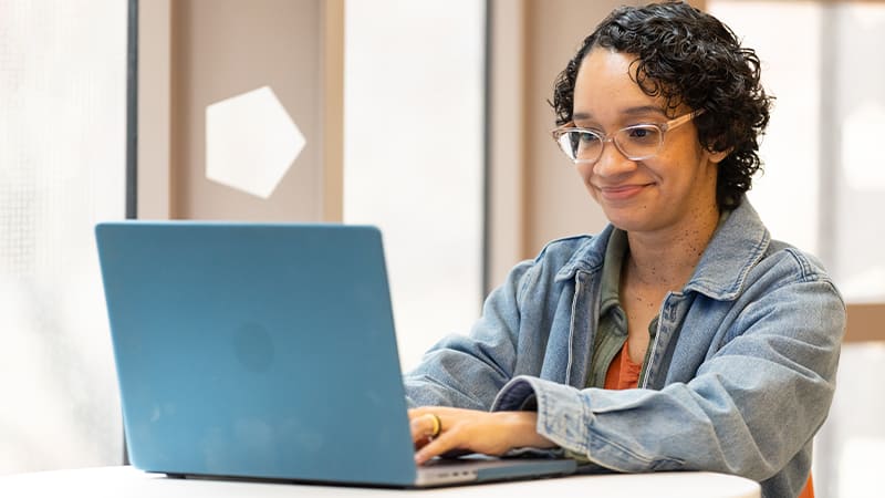 Michelle Littlejohn, who earned her online degree from SNHU in 2024, wearing a denim jacket and typing on her laptop.
