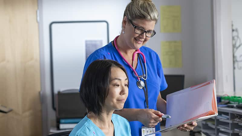 Kristina Libby, who earned her nursing degree from SNHU in 2017, wearing blue scrubs and holding a clipboard next to a colleague in a clinical office.