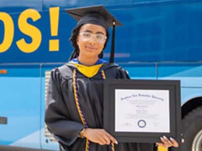 Ashley Figueroa, a 2023 SNHU graduate who earned her bachelor's in computer science holding her diploma in front of the SNHU bus.