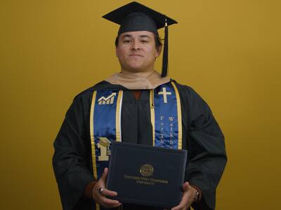 Kevin Bucardo '26 MBA, an SNHU MBA in Finance graduate, wearing his graduation cap and gown while holding his diploma.