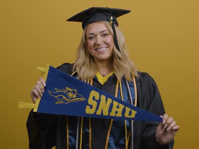 Madison Richards '26, a graduate of SNHU's Bachelor of Science in Marketing with a concentration in Digital Marketing, wearing her cap and gown and holding an SNHU pennant.