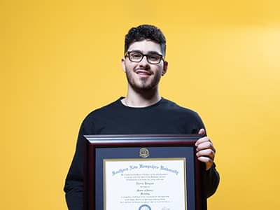 Naeem Jaraysi, who earned his online master's in marketing in 2020, holding his framed diploma.