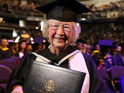 Annette Roberge '24, who earned her associate degree in business administration from SNHU, wearing her cap and gown and holding her diploma.