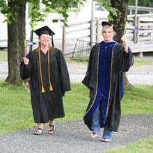Long-time friends Fiona Mathiesen and Dr. Gwen Britton, dressed in graduation regalia, holding SNHU pennants.