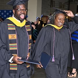 Two graduates in caps and gowns, exiting the SNHU Commencement ceremony together