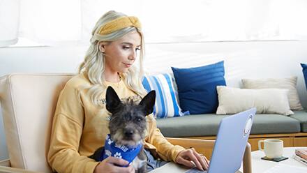 An SNHU student with their dog, sitting down while using a laptop.