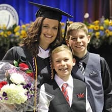 Tara Theis dressed in a graduation cap and gown and to the left of two sons