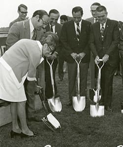 Gertrude Shaprio and a group of men in suits using shovels to break ground on SNHU's campus.
