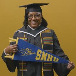 Valerie Craig, a 2025 graduate from SNHU dressed in a cap and gown and holding an SNHU pennant.