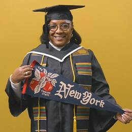 Valerie Craig, a 2025 graduate from SNHU dressed in a cap and gown and holding a New York state pennant.