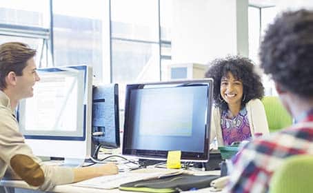 3 people talking while working on computers