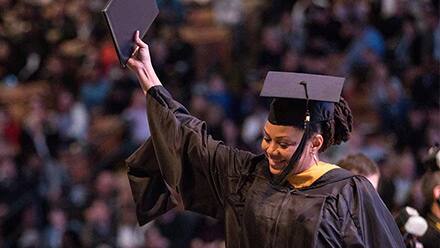 A graduate wearing a cap and gown, holding up her diploma at an SNHU Commencement ceremony