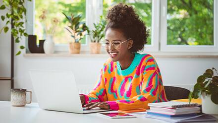 An undergraduate student wearing a bright orange shirt, completing her accelerated master's program coursework on a laptop