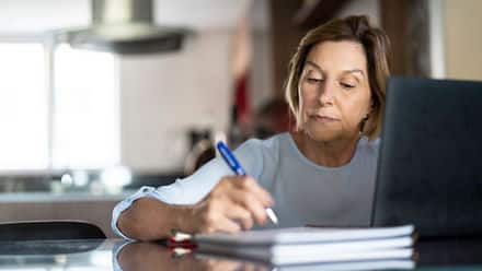 A person researching how to go back to college on a laptop and taking notes with a pen.