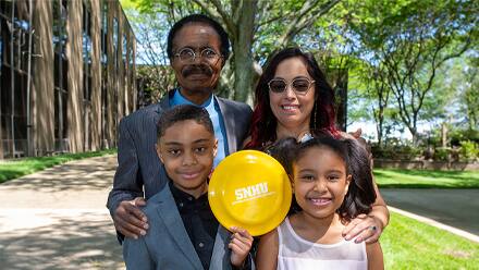 Davis Balogun standing with his family and holding an SNHU frisbee