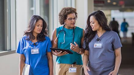Three nurses at different career levels walking in a hospital corridor.