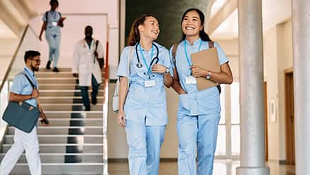 Two nurses dressed in scrubs and carrying backpacks for the class they're getting continuing education credits from.