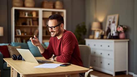 A man sitting at a desk smiling and working on his laptop while earning an English degree.