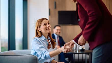 A professionally dressed woman shaking someone's hand in an office setting to represent entry-level HR jobs.