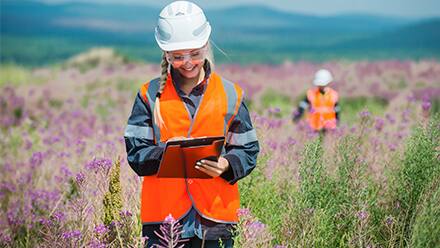 Environmental scientists in a field wearing protective equipment and taking notes.