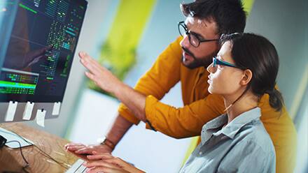 A student getting experiential learning in programming with the support of a professional who is pointing at the computer.