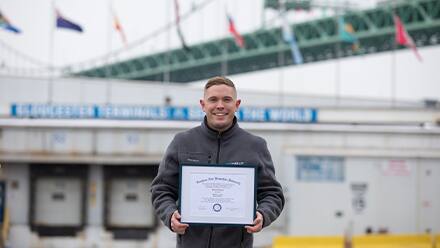 Rob Thomas, a 2024 SNHU graduate holding his diploma standing outside in an industrial area.