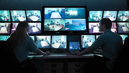 Two homeland security professionals monitoring a series of security camera feeds