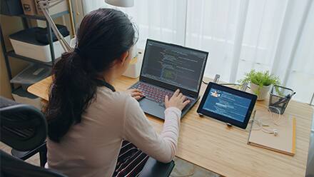 A computer science master's student programming on a laptop with a tablet next to it.