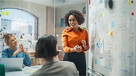 A marketing manager presenting ideas on a whiteboard during a team meeting while colleagues listen.