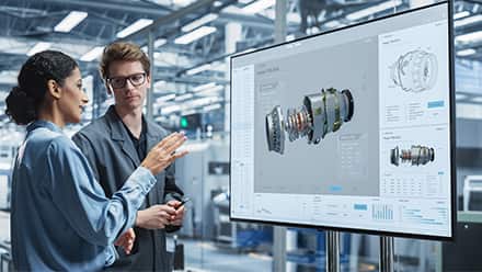 An engineering manager listening to an engineer explaining machinery on a screen.