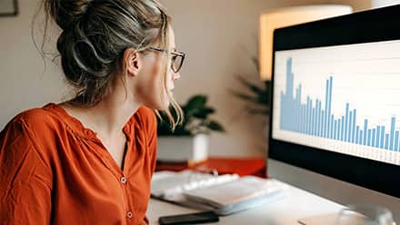 A professional who learned how to become a data analyst, sitting in front of a computer with a bar graph on the screen.
