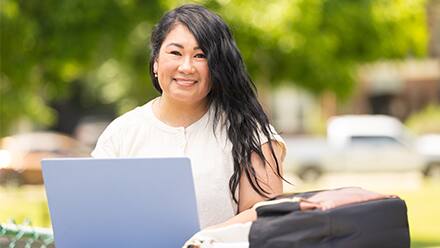 A student choosing a college on her laptop while outdoors.