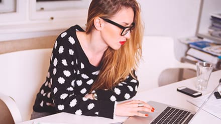 A woman sitting at a desk using a laptop to research how to get a scholarship.