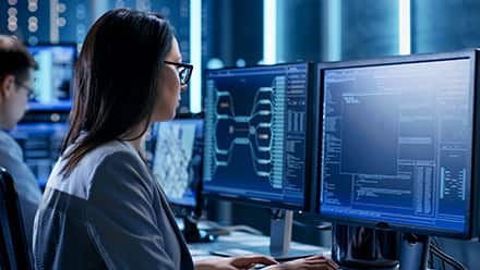 A woman sitting in front of two computer monitors after she learned how to become a cyber security professional.