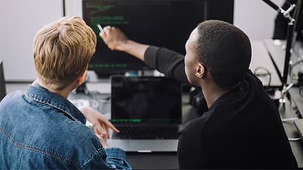 An instructor looking at code on a computer with a student who wants to get into tech.