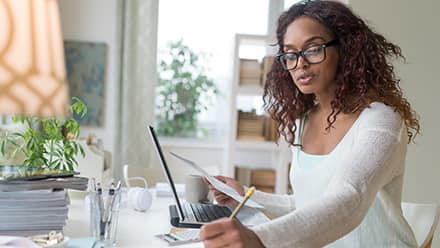 A person at a table, reviewing documents and taking notes in a notebook on how to get a master's degree.
